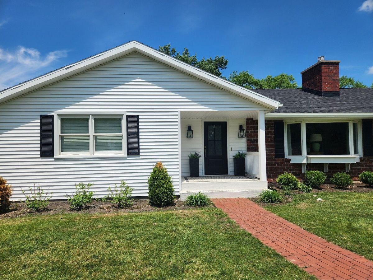 White ranch home with black shutters, a covered front entry and brick walkway
